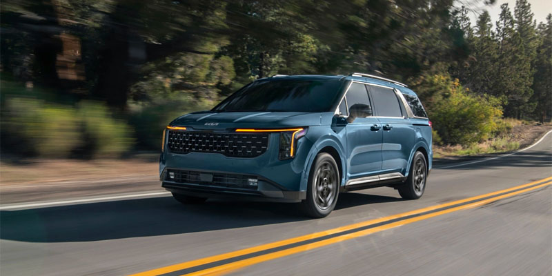 A blue 2025 Kia Carnival driving down a paved road