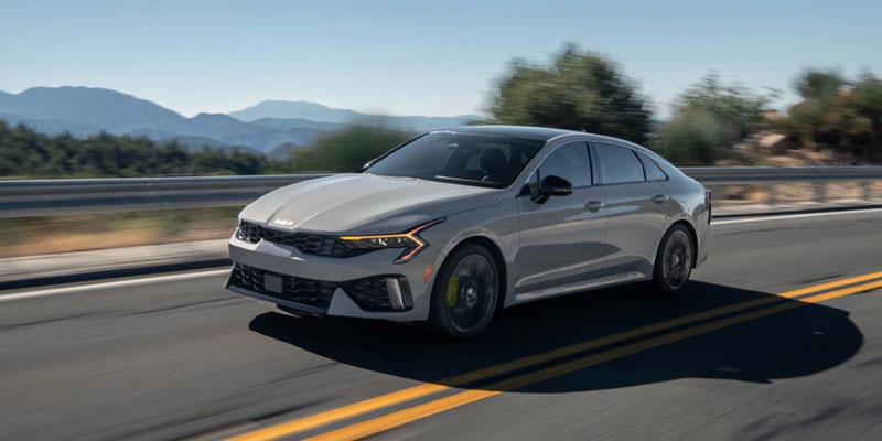 a grey 2025 Kia K5 driving down a paved road