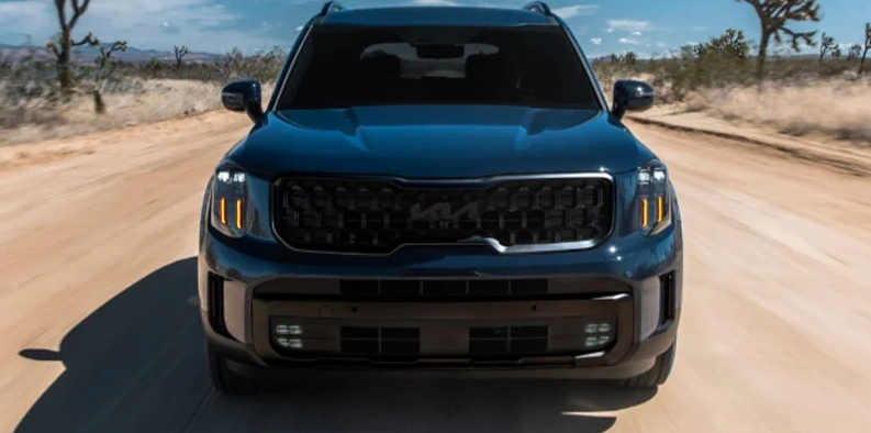 A photo of a black 2025 Kia Telluride driving down a dirt road.