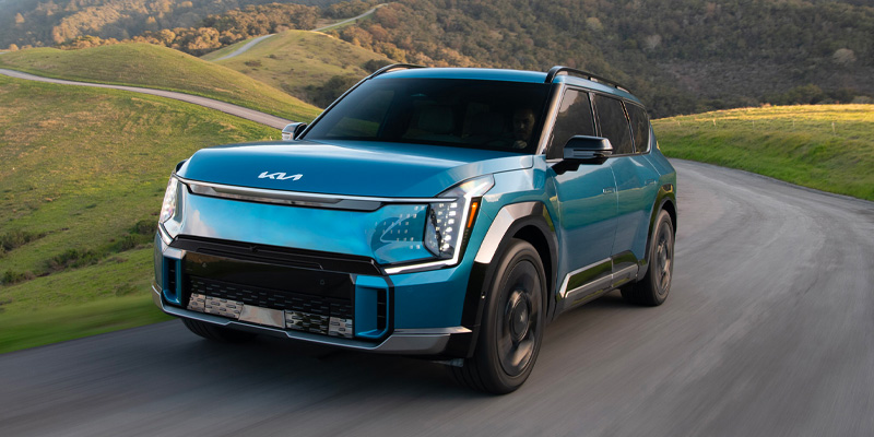 a blue 2025 Kia EV9 driving down a road